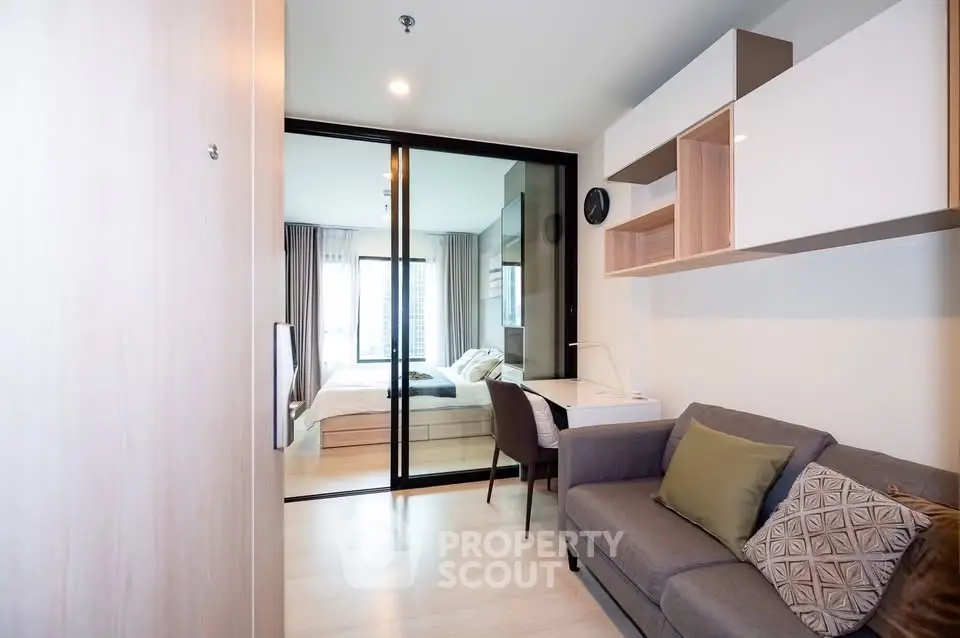 Modern studio apartment with cozy living area and stylish bedroom separated by glass doors.