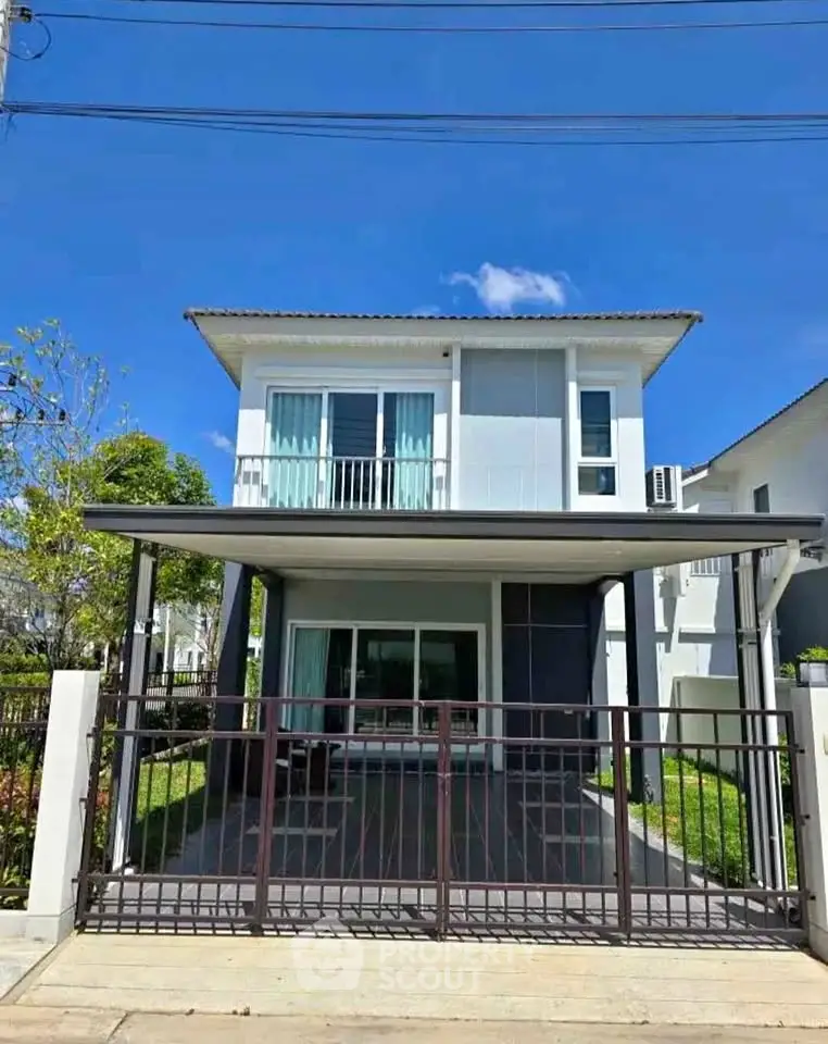 Modern two-story house with gated entrance and balcony under clear blue sky.