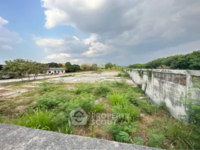 Expansive vacant land with lush greenery and potential for development under a cloudy sky.