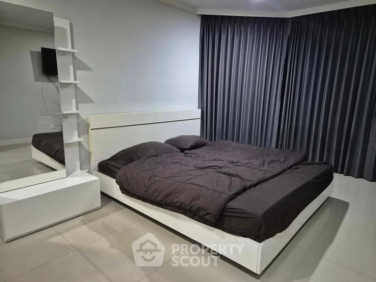 Modern bedroom with sleek design and dark curtains, featuring a minimalist bed and wall-mounted TV.