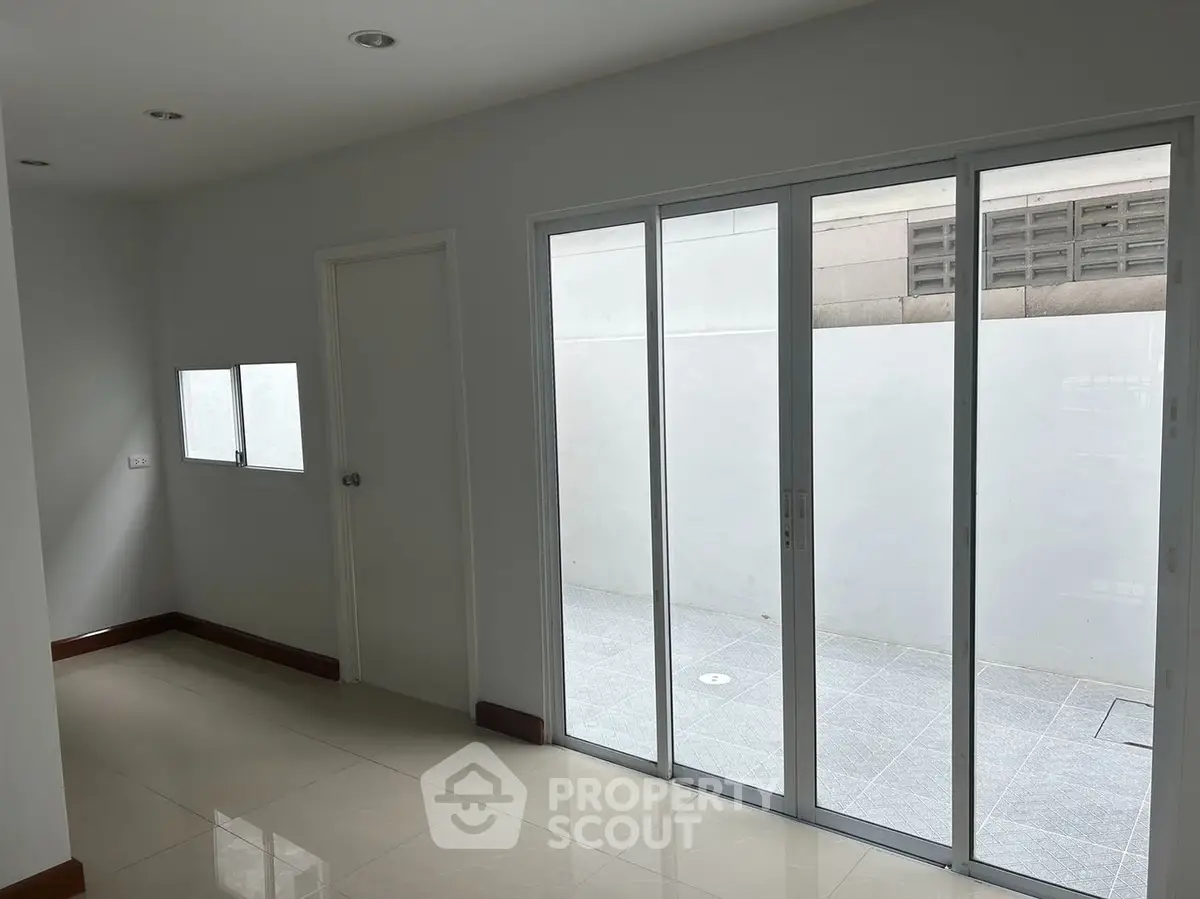 Spacious and bright room with large sliding glass doors leading to a private patio, featuring glossy tiled flooring and a fresh, clean white wall palette.