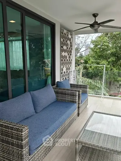 Spacious balcony with modern wicker furniture and lush greenery view, perfect for relaxation.