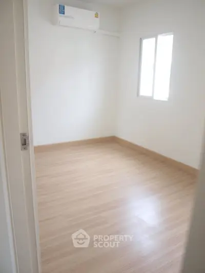 Bright empty room with wooden flooring and air conditioning, perfect for customization.