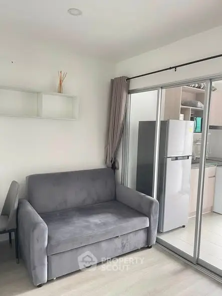 Modern living room with sleek gray sofa and kitchen view, featuring sliding glass doors for natural light.