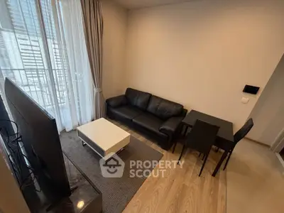 Modern living room with sleek black sofa, flat-screen TV, and dining area in a stylish apartment.