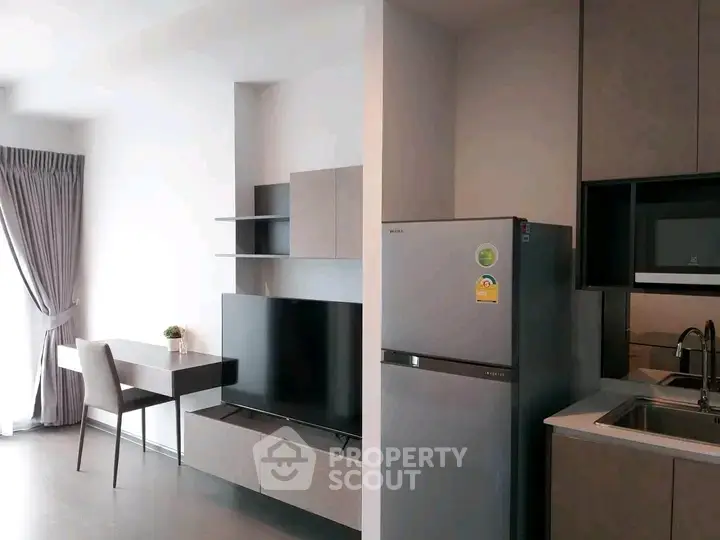 Modern apartment interior with sleek kitchen and living area featuring a TV and fridge.
