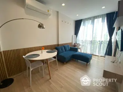 Modern living room with stylish blue sofa and dining area, featuring large windows and natural light.