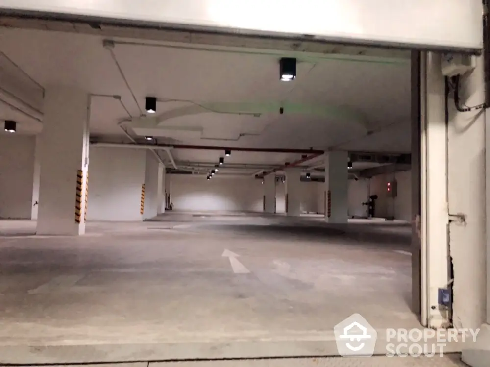 Spacious underground parking facility in a modern residential building, featuring ample lighting and clear directional markings.