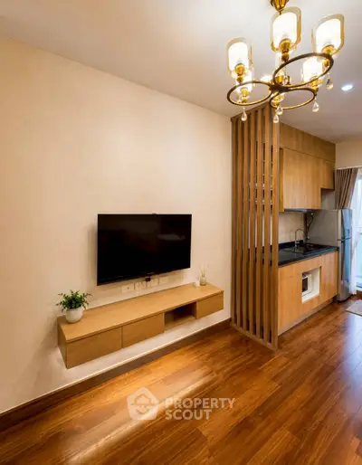 Modern living room with wooden flooring and open kitchen layout, featuring elegant lighting and wall-mounted TV.
