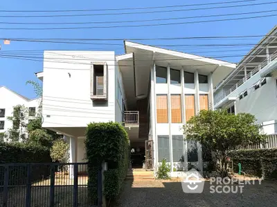 Modern two-story house with unique architecture and lush greenery in a serene neighborhood.