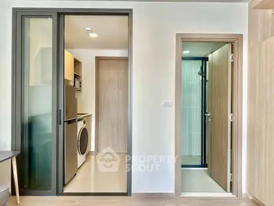 Modern apartment interior with sliding door, washing machine, and sleek bathroom entrance.