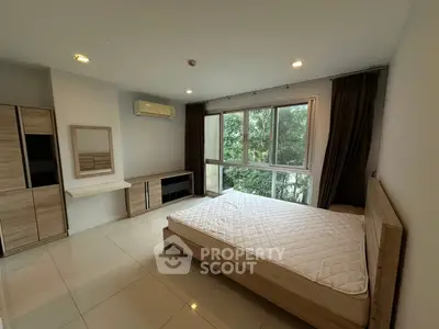 Spacious bedroom with large window and modern furnishings, offering a serene view of greenery.