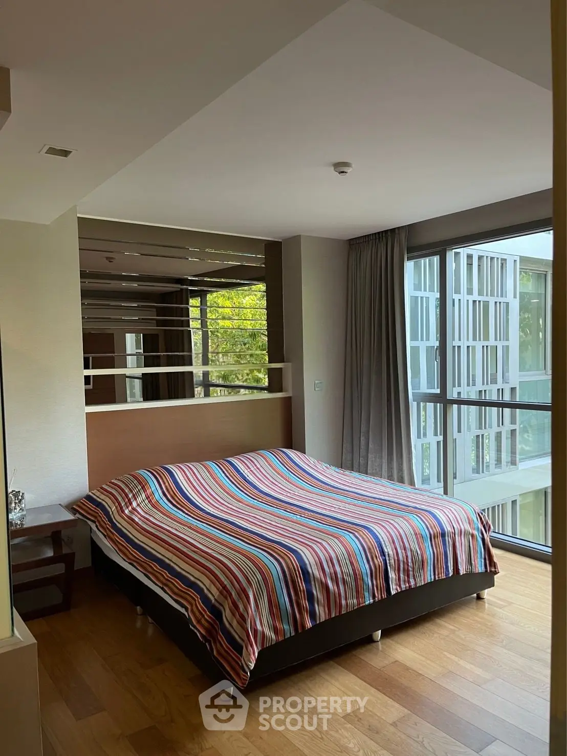 Modern bedroom with large windows and striped bedding in a stylish apartment.