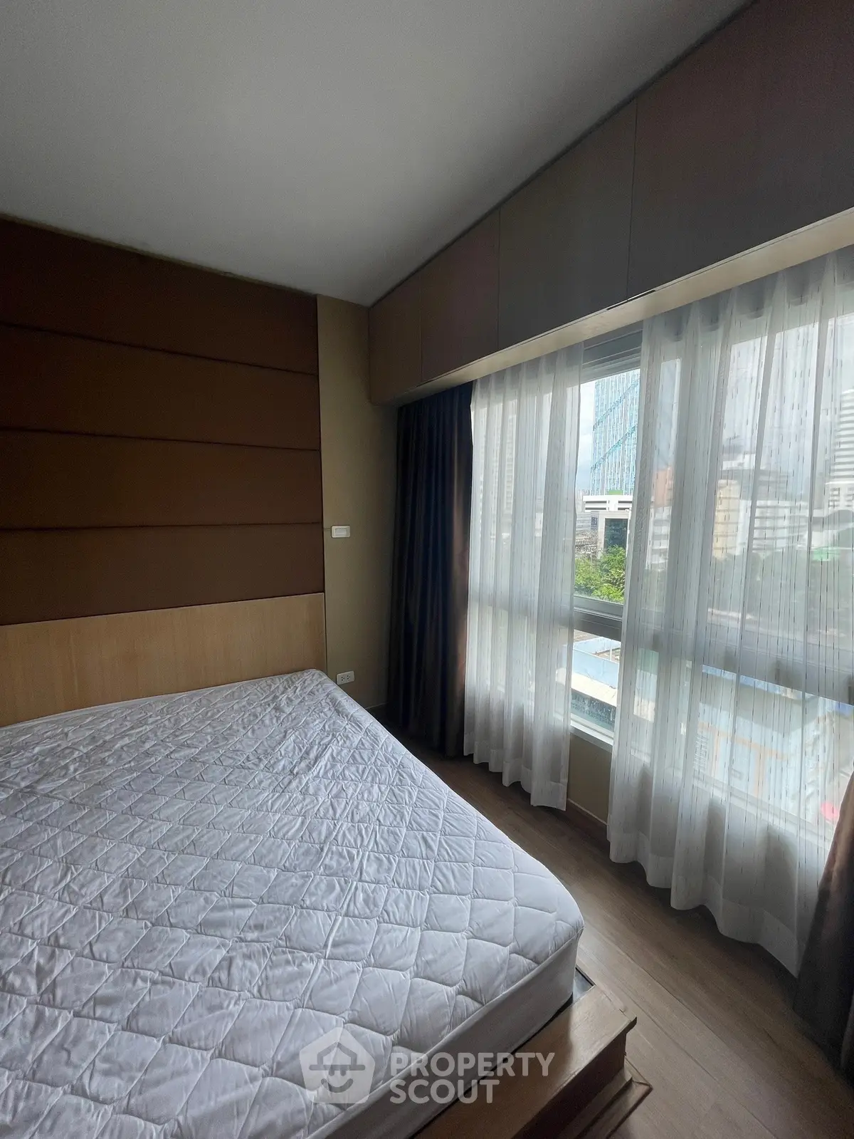 Spacious bedroom with large window offering city view, featuring modern design and ample natural light.
