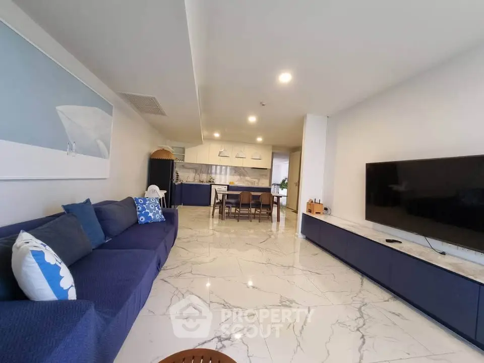 Spacious modern living room with open kitchen, marble floors, and sleek blue furniture.