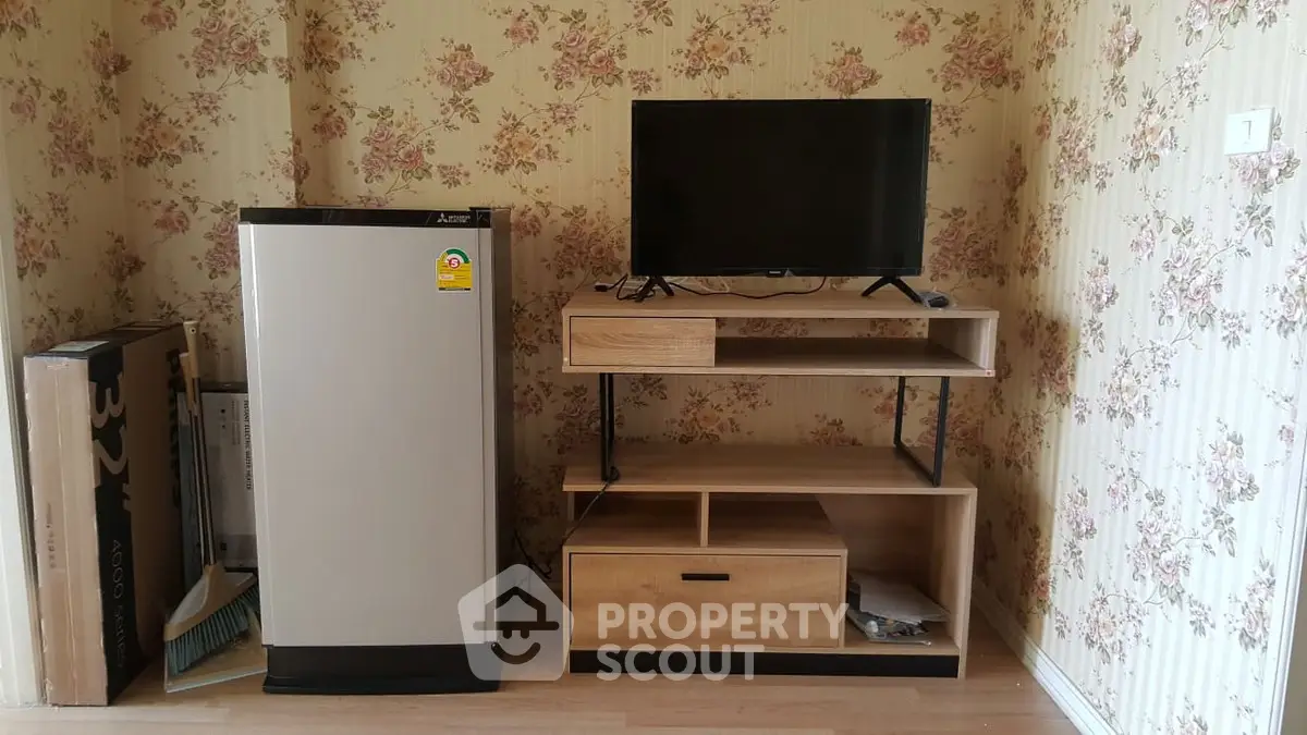 Cozy living room corner with TV stand and compact fridge, floral wallpaper adds charm.