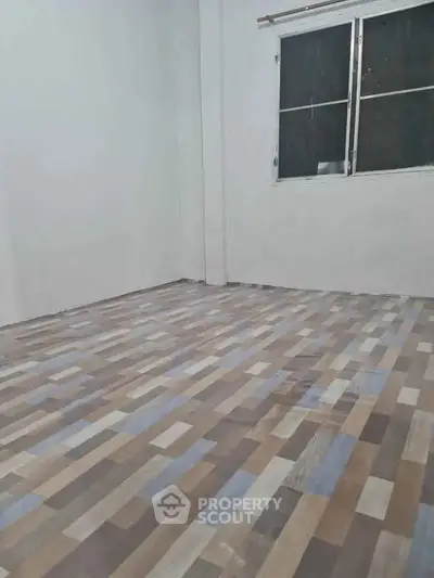 Spacious empty room with modern wood-patterned flooring and large window.