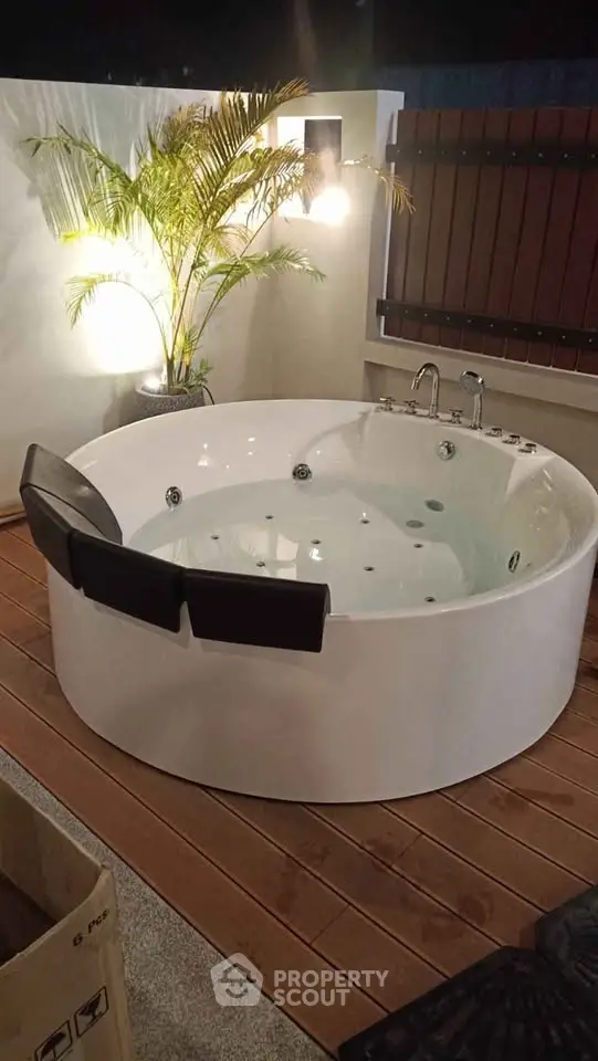 Luxurious outdoor jacuzzi on a stylish wooden deck with ambient lighting and lush greenery.