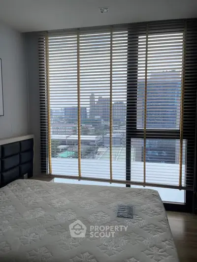 Modern bedroom with large window offering stunning city view, featuring sleek blinds and stylish decor.