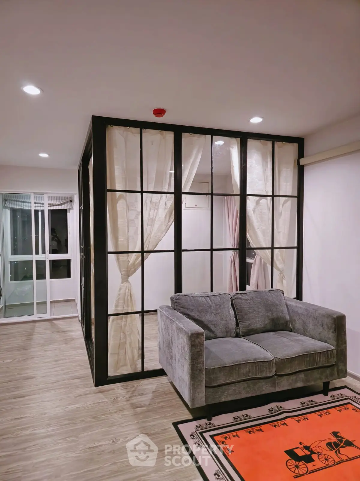 Modern living room with glass partition and cozy gray sofa, featuring elegant curtains and stylish decor.