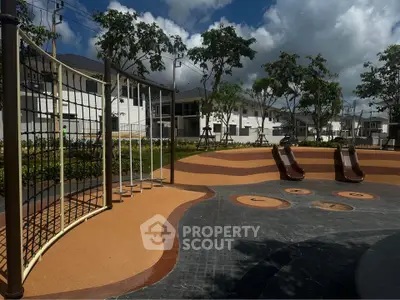 Modern residential playground with slides and climbing net under a cloudy sky.