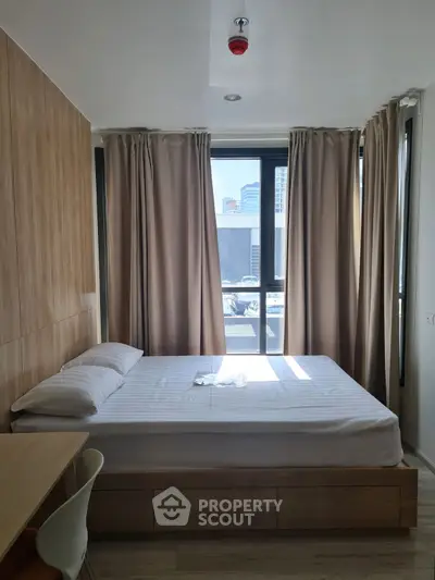 Modern bedroom with large window and city view, featuring a cozy bed and wooden accents.
