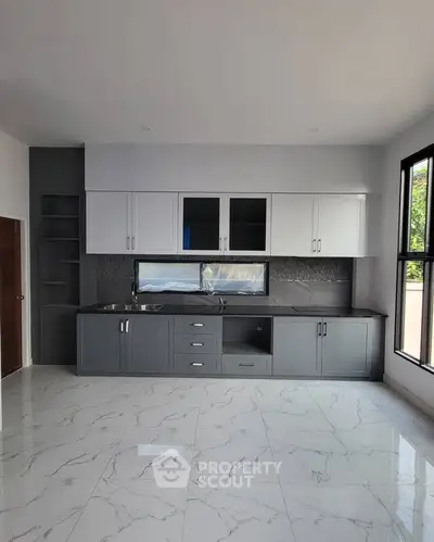 Modern kitchen with sleek cabinetry and marble flooring, featuring large windows for natural light.