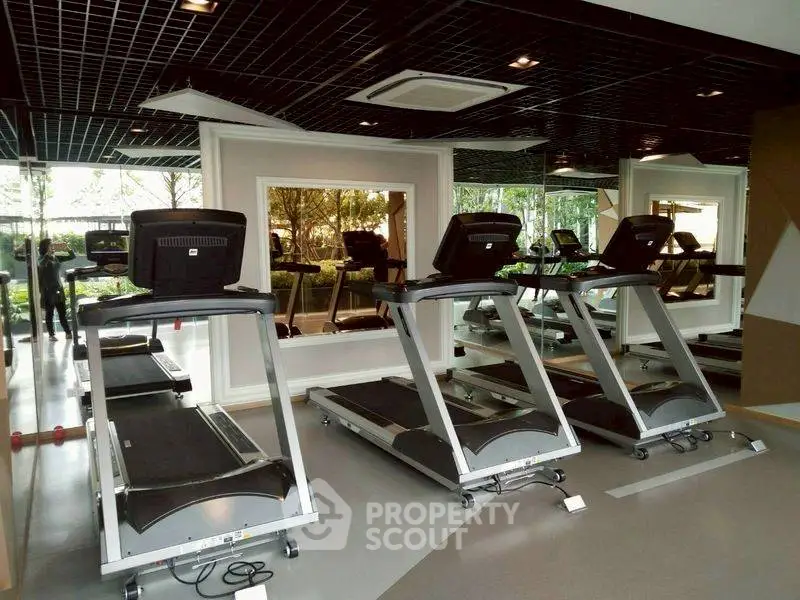 Modern gym with multiple treadmills and mirrored walls in luxury apartment complex.