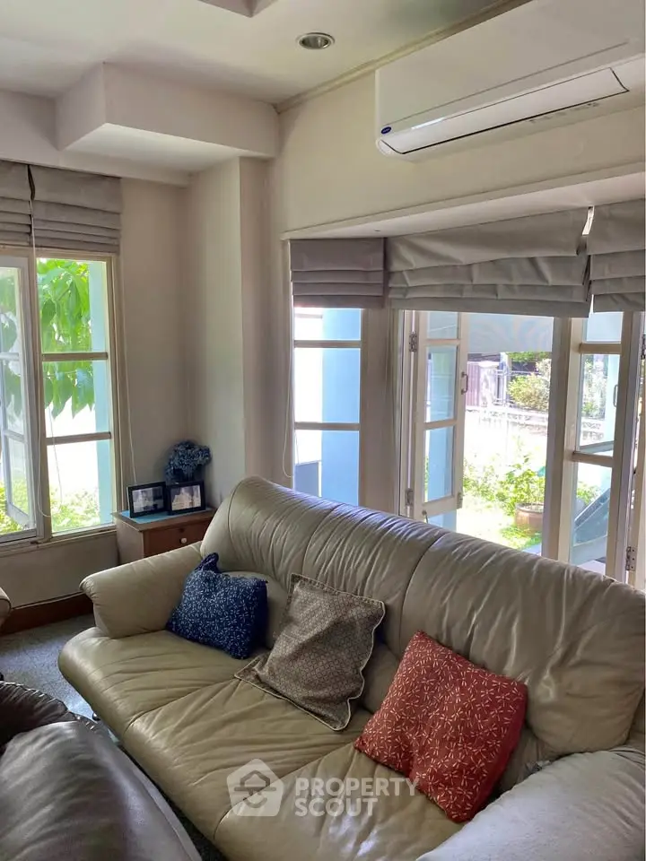 Cozy living room with leather sofa and large windows offering natural light and garden view.