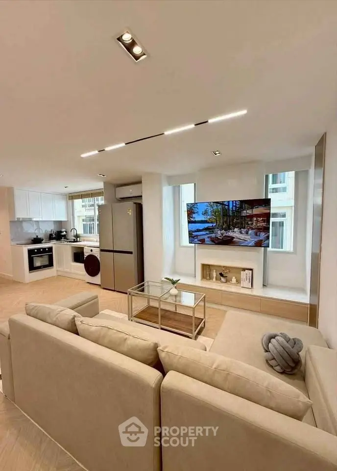 Modern open-plan living room with sleek kitchen and large TV, perfect for entertaining.