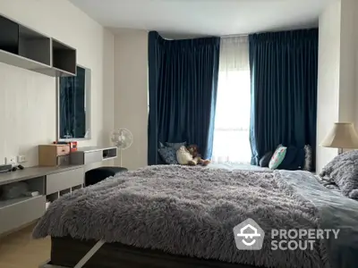 Cozy bedroom with plush bedding and modern decor, featuring a large window with dark curtains.