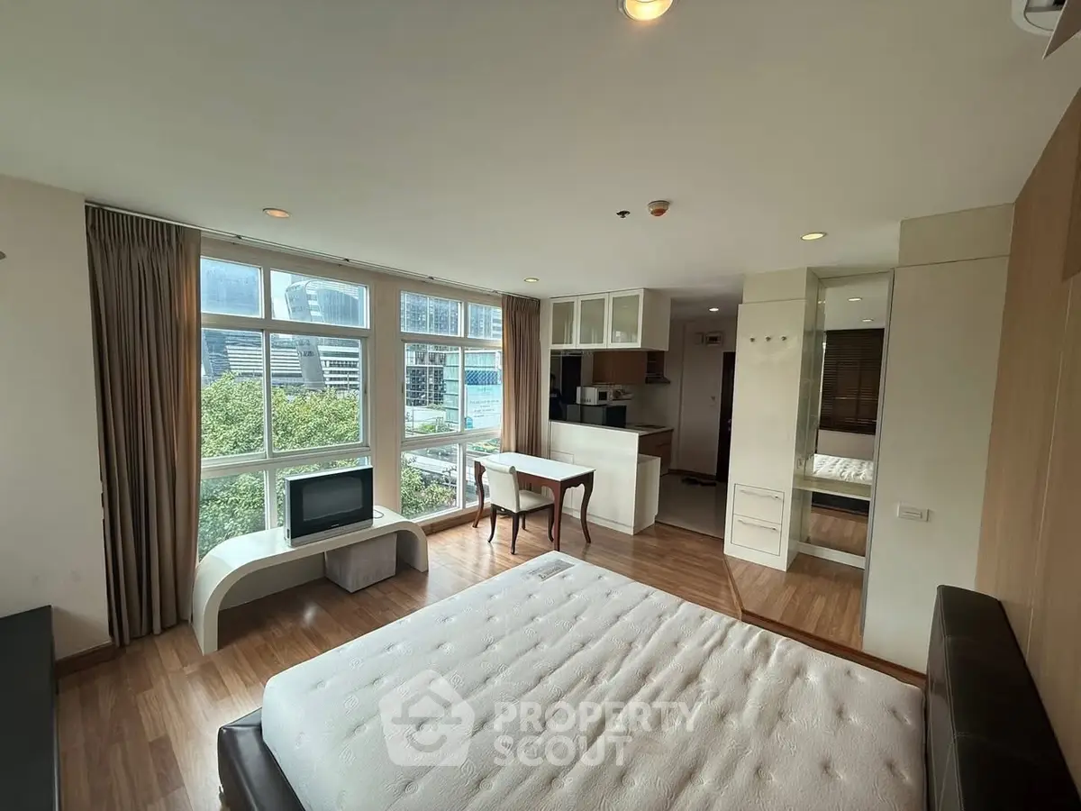 Spacious studio apartment with large windows and city view, featuring modern furnishings and open layout.