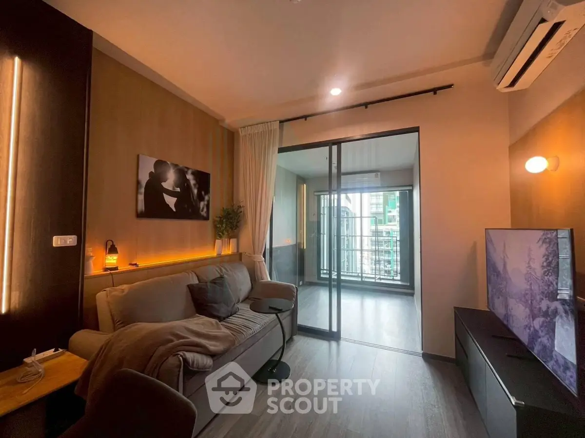 Modern living room with cozy sofa and large TV, leading to a glass-enclosed balcony with city view.