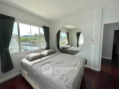 Spacious bedroom with large window and round mirror, offering serene views.