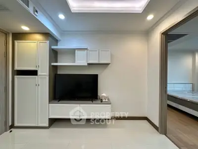 Modern living room with sleek white cabinetry and mounted TV, leading to a cozy bedroom.