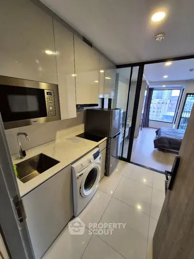 Modern compact kitchen with washing machine and view into bedroom in urban apartment.