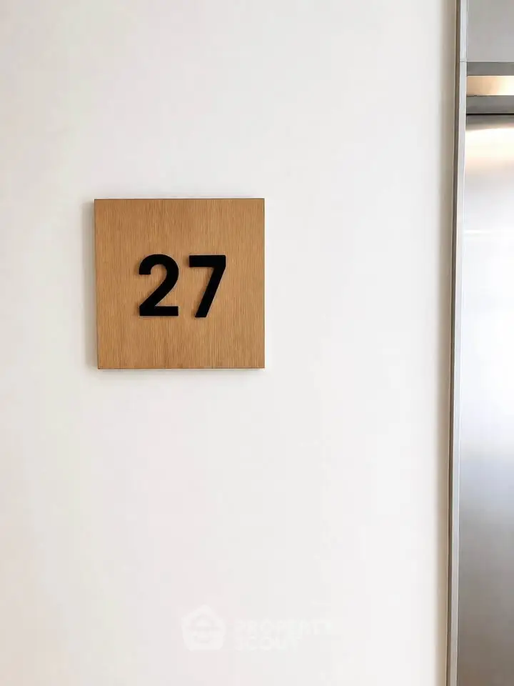 Modern elevator lobby with stylish room number 27 on wooden plaque.