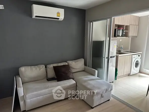 Modern living room with cozy sofa and adjacent kitchen featuring appliances.