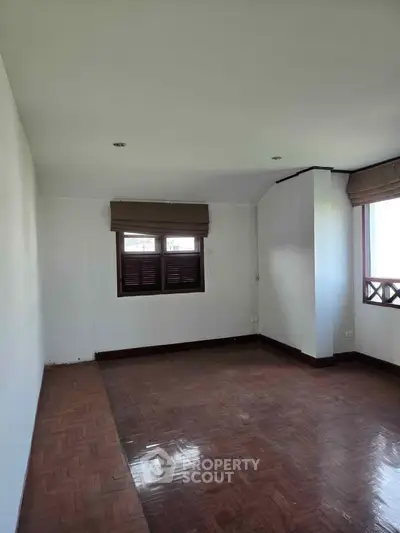 Spacious empty room with wooden flooring and large windows, perfect for customization.