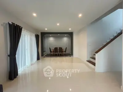 Spacious modern living room with elegant dining area and staircase, featuring sleek tile flooring and ambient lighting.