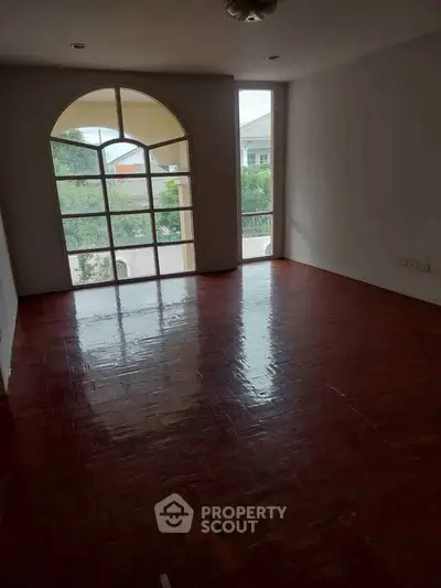 Spacious empty room with large arched window and polished wooden floor.