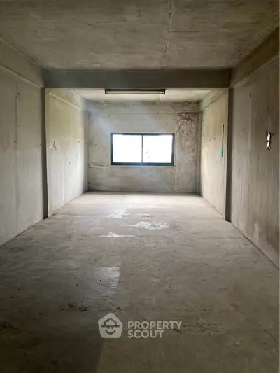 Spacious unfinished room with concrete walls and large window, ideal for customization.