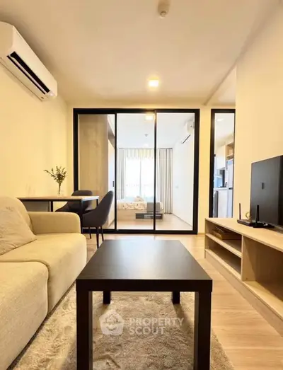 Modern living room with open layout, cozy sofa, and view into a stylish bedroom through glass doors.