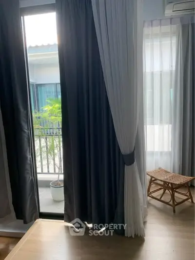 Cozy bedroom with natural light and balcony access, featuring elegant curtains and wooden flooring.