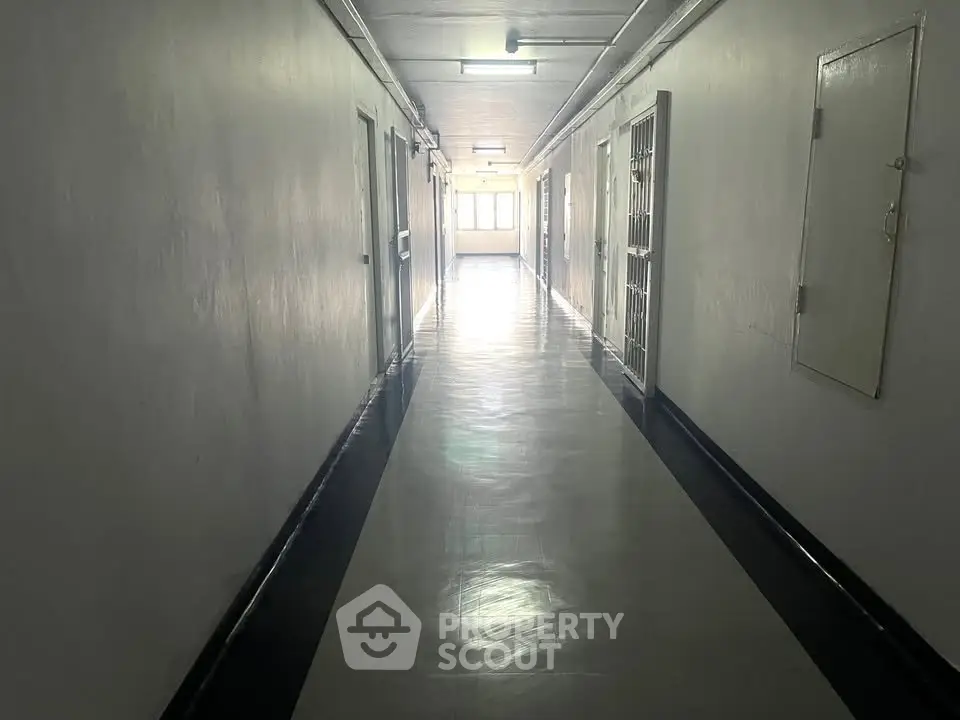 Spacious and well-lit corridor in a residential building with polished floors and bright lighting.