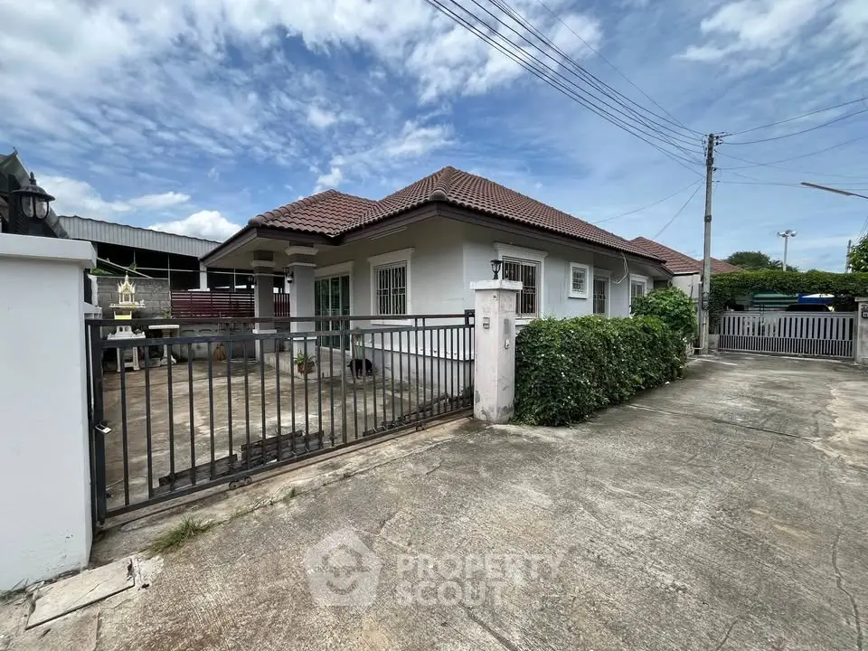 Charming single-story house with gated driveway and lush greenery under a clear blue sky.