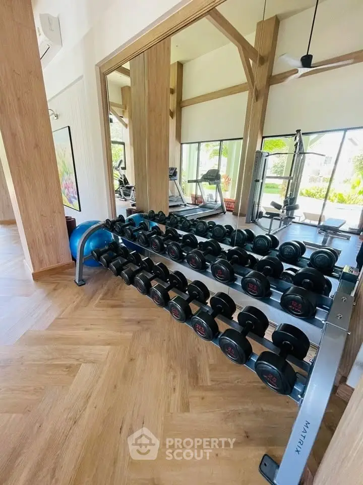 Modern gym with mirrored walls and wooden flooring in luxury real estate property.