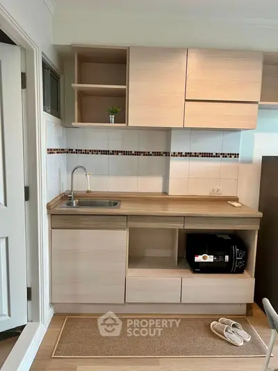 Modern compact kitchen with wooden cabinets and microwave, ideal for small apartments.