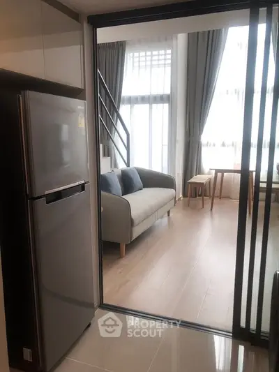 Modern apartment with open layout, featuring a cozy living room and sleek kitchen with stainless steel fridge.