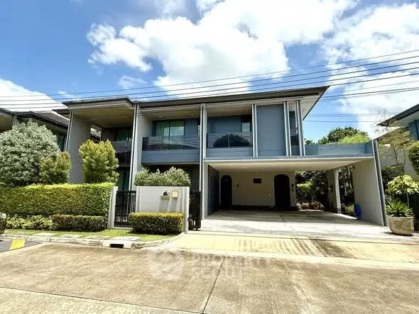 Modern two-story house with spacious driveway and lush greenery under a clear blue sky.